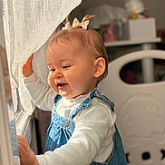 Haïvie participe au concours pour gagner de l'argent avec cette photo : baby, child, infant, smile, overalls, denim_overalls, white_shirt, hair_bow, curtain, window, sunlight, indoor, crib, bokeh, portrait, hand, face, cheeks, playful, happy