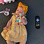 baby, child, colorful, cute, dress, floor_mat, headband, indoors, infant, lying_down, pacifier, person, playtime, plush_toy, remote_control, sock, soft_toys, striped_clothing, toy, yellow