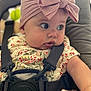 baby, child, headband, bow, car_seat, seatbelt, floral_dress, cute, infant, face, portrait, chubby_cheeks, wide_eyes, soft_light, indoors, straps, clothing, person, closeup, curious