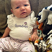 Oakley joined the competition — help win amazing prizes! baby, blanket, blue_eyes, child, clothing, comfort, couch, expression, fabric, face, hand, indoor, infant, patterned_pants, portrait, ruffled_sleeves, sitting, skin, text_on_clothing, texture