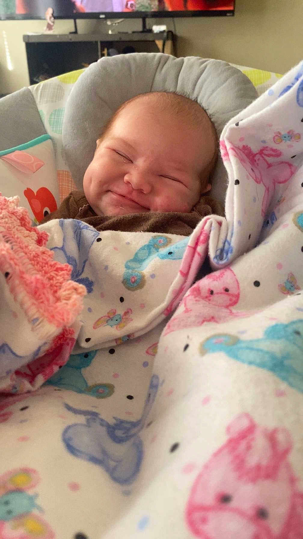 Oakley joined the competition — help win amazing prizes! baby, smiling, blanket, animal_print, cushion, infant, face, child, indoors, comfort, cute, happy, seated, soft_toys, warm, cozy, portrait, newborn, expression, clothing