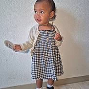 Nellya participe au concours pour gagner de l'argent avec cette photo : toddler, child, girl, dress, cardigan, shoes, socks, floor, wall, paper, curly_hair, standing, indoor, expression, looking_away, buttoned_dress, white_socks, black_shoes, plaid_pattern, light