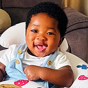 Kenechukwu is registered to the contest to win money with this photo: baby, smiling, happy, child, infant, overalls, white_shirt, baby_seat, indoor, cute, portrait, african_american, button, furniture, couch, face, one_person, young_child, baby_clothing, closeup