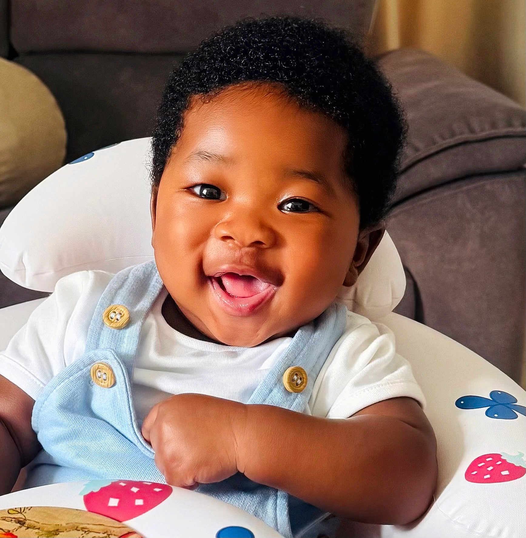 Kenechukwu is registered to the contest to win money with this photo: baby, smiling, happy, child, infant, overalls, white_shirt, baby_seat, indoor, cute, portrait, african_american, button, furniture, couch, face, one_person, young_child, baby_clothing, closeup