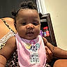 Loyal is registered to the contest to win money with this photo: baby, infant, child, portrait, sitting, indoors, pink_bib, floral_bib, pigtails, curly_hair, dark_skin, face, eyes, hands, adult, lap, leopard_print, kitchen, shelf, jar
