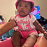 baby, child, infant, portrait, pink_hat, bucket_hat, pink_clothing, striped_shirt, sitting, curious, face, eyes, indoor, living_room, television, adult, arm, furniture, colorful, family