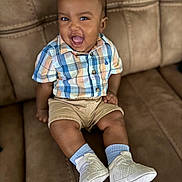 Cairo joined the competition — help win amazing prizes! baby, child, smiling, plaid_shirt, khaki_shorts, white_sneakers, blue_socks, sitting, couch, indoor, happy, portrait, cute, young_child, person, fashion, footwear, clothing, infant, expression
