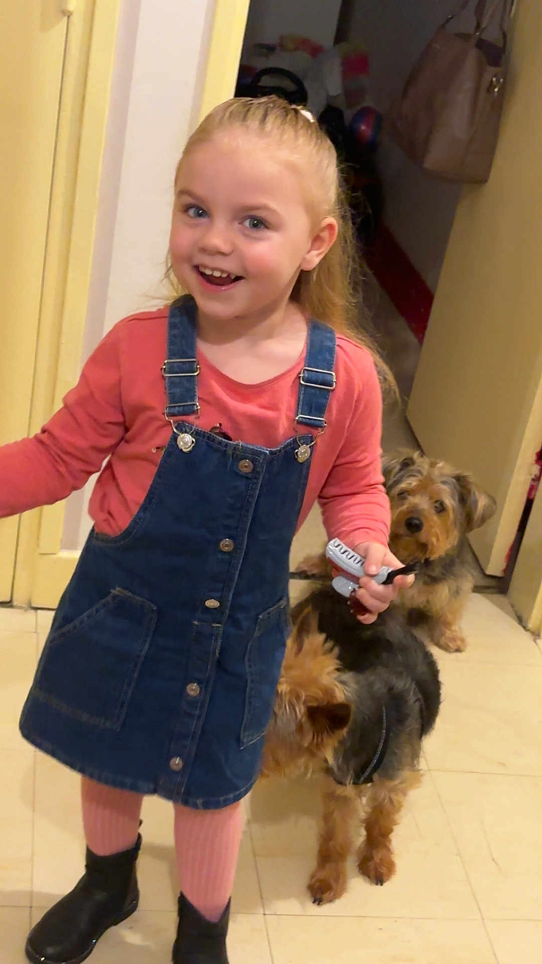 Zoe a rejoint le concours — aidez-le/la à gagner de superbes lots ! child, girl, smiling, indoor, denim_dress, pink_tights, black_boots, toy, hairbrush, dog, two_dogs, floor, doorway, happy, person, pet, animal, home, curly_hair, playful