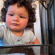 Emir joined the competition — help win amazing prizes! child, toddler, curly_hair, indoor, portrait, person, face, expression, clothing, short_sleeve, table, reflection, curiosity, skin, red_cheeks, background, curtains, window, light, casual