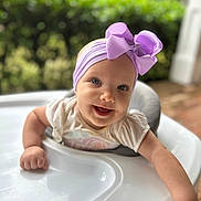 Ann-Elaine is registered to the contest to win money with this photo: baby, infant, child, smiling, happy, face, portrait, high_chair, bow, headband, lavender, clothing, white_shirt, sitting, outdoor, garden, greenery, natural_light, tray, close_up