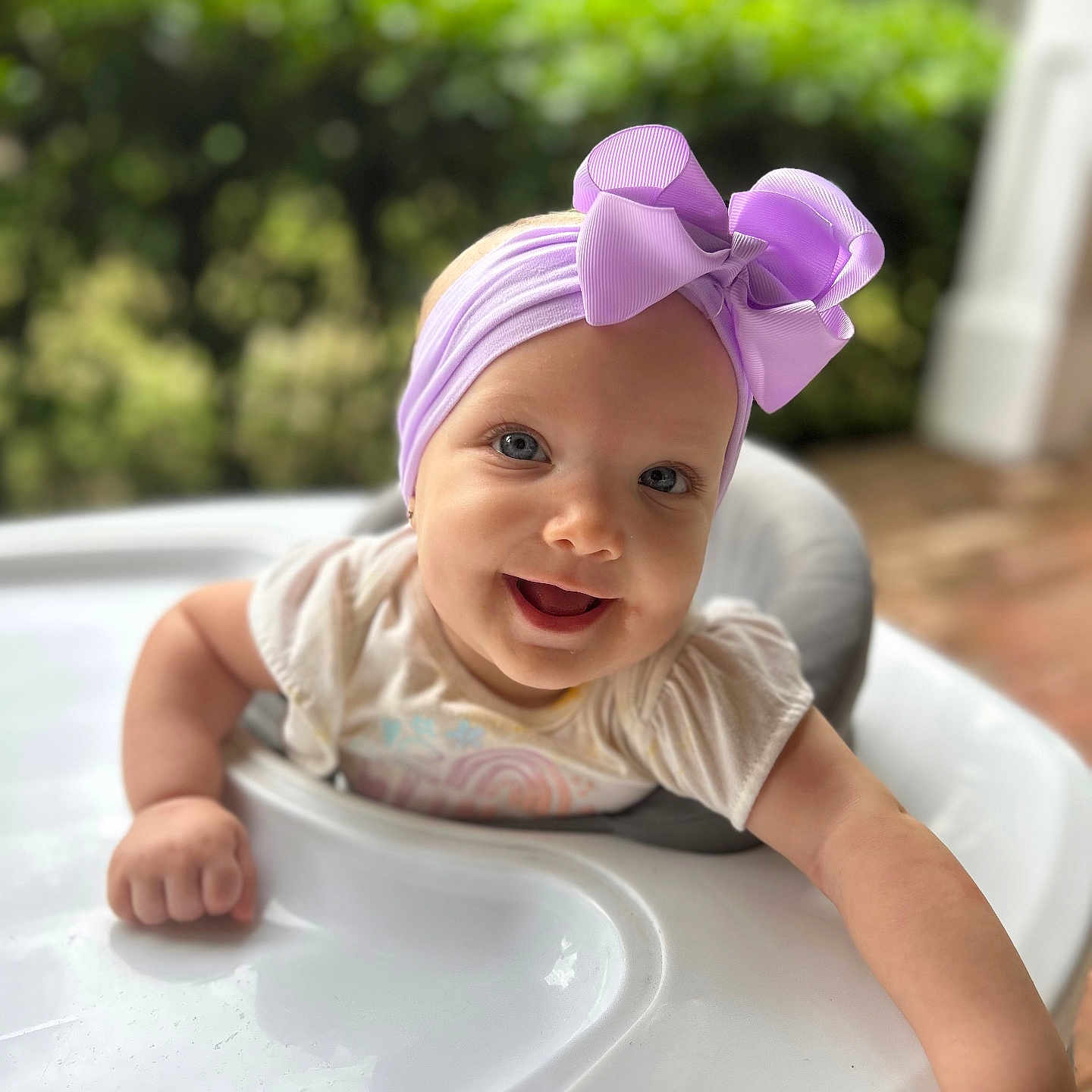 Ann-Elaine is registered to the contest to win money with this photo: baby, infant, child, smiling, happy, face, portrait, high_chair, bow, headband, lavender, clothing, white_shirt, sitting, outdoor, garden, greenery, natural_light, tray, close_up