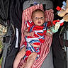 baby, infant, stroller, blanket, striped_blanket, toy, colorful_clothing, watermelon_pattern, outdoor, legs, face, hand, soft_toy, fabric, comfort, cute, child, person, resting, casual