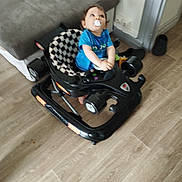 Joseph a rejoint le concours — aidez-le/la à gagner de superbes lots ! baby, child, walker, pacifier, blue_shirt, indoor, floor, couch, slippers, wooden_floor, toy, person, home, furniture, seat, black, white, checkered, looking_up, blur