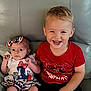 Rosalyn is registered to the contest to win money with this photo: baby, toddler, child, smiling, happy, sitting, couch, leather, clothing, red_shirt, headband, bow, face, portrait, indoor, celebration, fireworks_design, cute, people, two_children