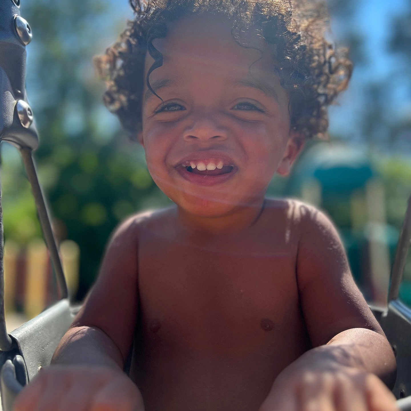 Orienn is registered to the contest to win money with this photo: bare_chest, blurred_background, child, curly_hair, daylight, fun, hands, happy, joy, nature, outdoor, park, play, playground, portrait, smiling, sunlight, swing, toddler, young_child