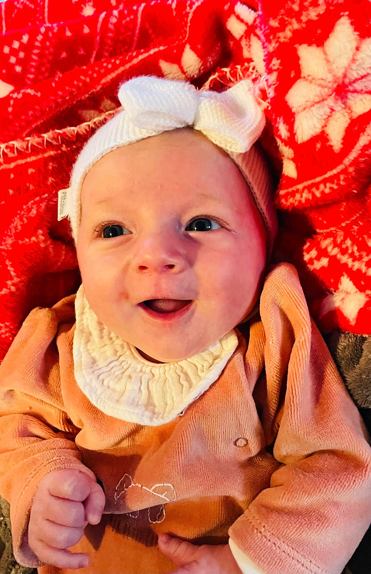 Luna a rejoint le concours — aidez-le/la à gagner de superbes lots ! baby, smile, headband, bow, red_blanket, pattern, orange_clothing, infant, happy, cute, child, portrait, cozy, closeup, face, hands, warm, soft, indoors, newborn