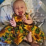 baby, child, smiling, laughing, dress, sunflower_pattern, blanket, seat, indoors, footwear_absent, happy, infant, person, clothing, cute, sitting, head, face, joy, comfort