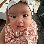 Lily is registered to the contest to win money with this photo: adorable, baby, big_eyes, bow, carpet, chubby_cheeks, closeup, coffee_table, couch, floral_pattern, hand, headband, indoor, infant, living_room, pink_outfit, portrait, sitting, toy_truck, wooden_floor
