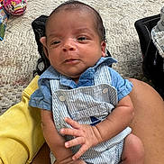 Julian is registered to the contest to win money with this photo: baby, infant, child, person, clothing, overalls, blue_shirt, hand, fingers, carpet, toy, indoor, sitting, skin, holding, cute, small, young, face, expression