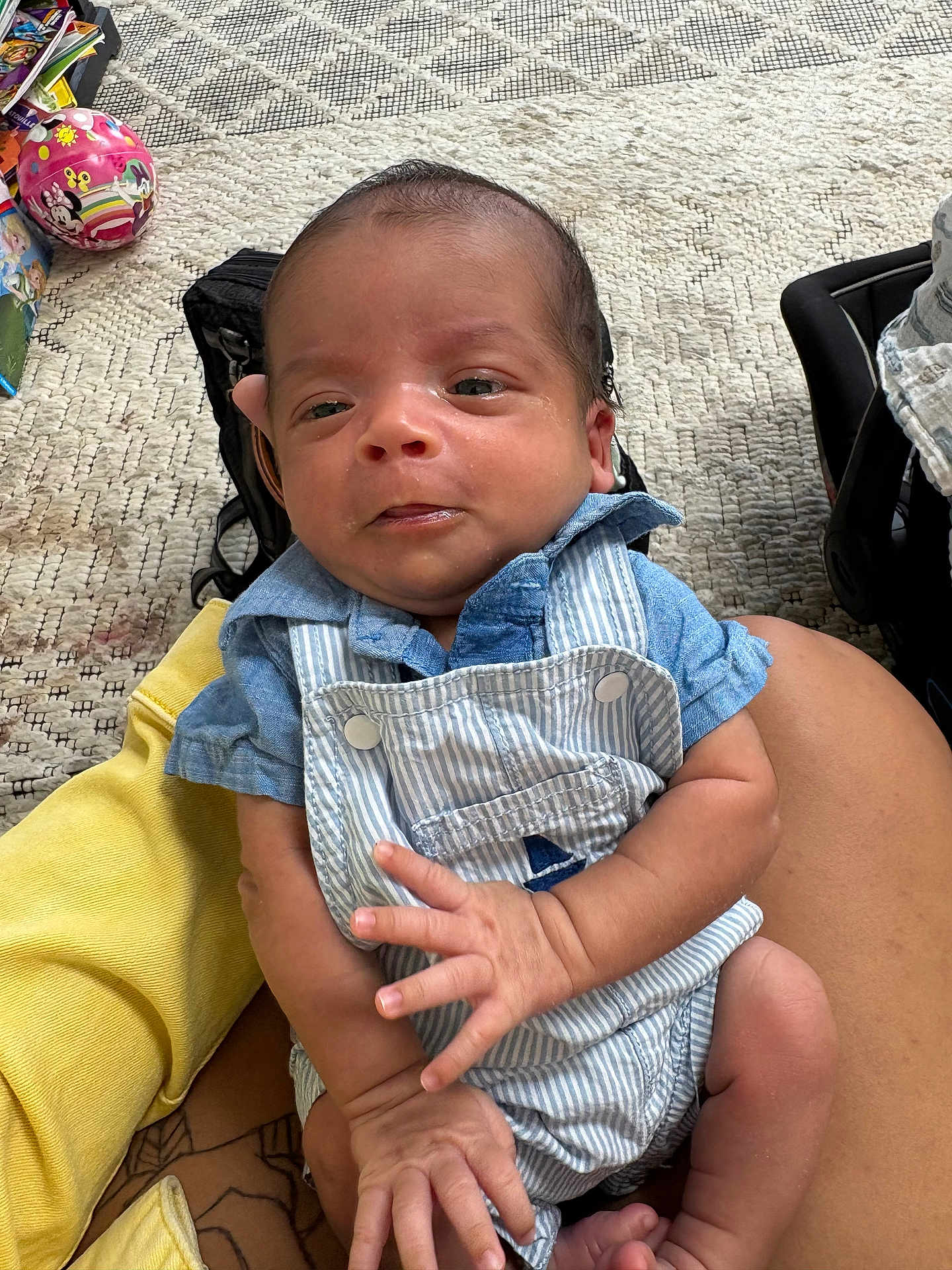 Julian is registered to the contest to win money with this photo: baby, infant, child, person, clothing, overalls, blue_shirt, hand, fingers, carpet, toy, indoor, sitting, skin, holding, cute, small, young, face, expression