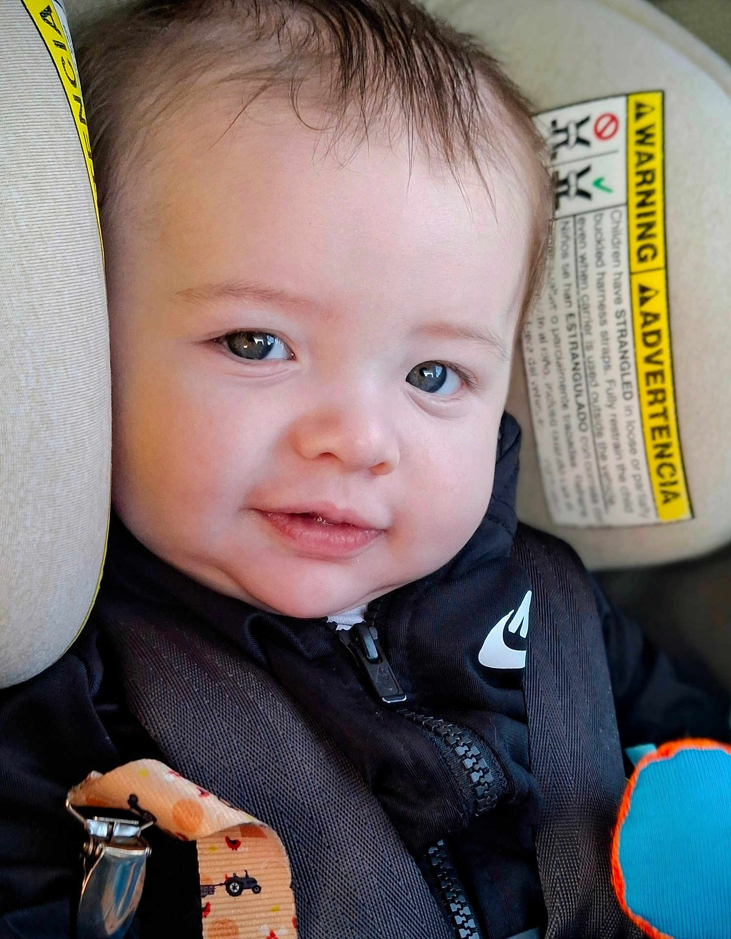 Haidyn joined the competition — help win amazing prizes! baby, child, face, smile, car_seat, seatbelt, clothing, zipper, toy, warning_label, black_jacket, infant, closeup, straps, cute, indoors, young_child, person, happy, head