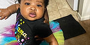 Truett is registered to the contest to win money with this photo: baby, child, tutu, headband, colorful, indoor, person, clothing, black_shirt, floor, carpet, tile, footwear, hand, arm, face, expression, holding, background, home