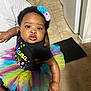 baby, child, tutu, headband, colorful, indoor, person, clothing, black_shirt, floor, carpet, tile, footwear, hand, arm, face, expression, holding, background, home