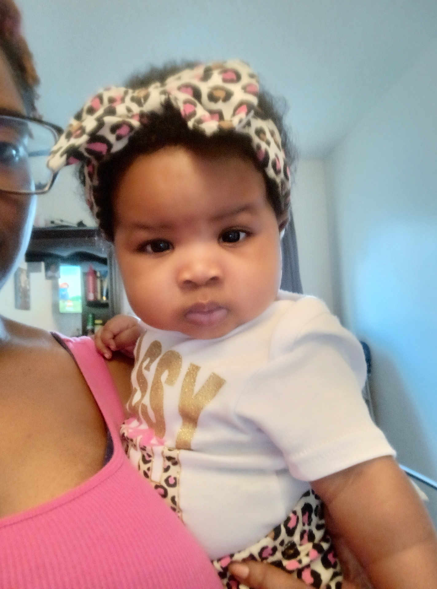 Truett joined the competition — help win amazing prizes! baby, child, headband, leopard_print, clothing, person, indoor, portrait, face, expression, holding, adult, glasses, pink_top, curly_hair, closeup, home, furniture, window, soft_light