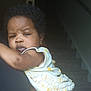 Truett is registered to the contest to win money with this photo: child, toddler, curly_hair, dress, white_clothing, yellow_pattern, arm, face, earring, indoor, staircase, person, serious_expression, skin, human, baby, portrait, holding, closeup, light