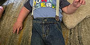Colton is registered to the contest to win money with this photo: toddler, child, carpet, pillow, suspenders, jeans, shirt, indoor, smiling, cute, baby, person, floor, head, face, hand, foot, clothing, relaxing, young