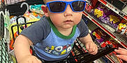 Colton joined the competition — help win amazing prizes! baby, blue_crocs, casual, child, clothing, cute, floor, hand, indoor, person, retail, shelf, shopping, shopping_cart, snacks, store, sunglasses, supermarket, toddler, toy