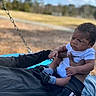 Jamari is registered to the contest to win money with this photo: toddler, child, outdoor, swing, sky, clouds, trees, park, grass, person, holding, baby, casual_clothing, daylight, expression, nature, recreation, playing, family, fun