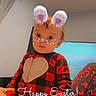 child, toddler, pajamas, indoor, digital_filter, bunny_ears, heart_shape, face_decoration, television, screen, patterned_clothing, red, black, plaid, sitting, holiday_text, easter, cute, young_child, portrait