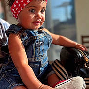Emmy joined the competition — help win amazing prizes! child, toddler, denim_overalls, headband, red_checkered, curly_hair, indoor, sunlight, portrait, cute, smiling, baby_shoes, hand, face, sitting, person, young_child, casual_clothing, table, background_blur