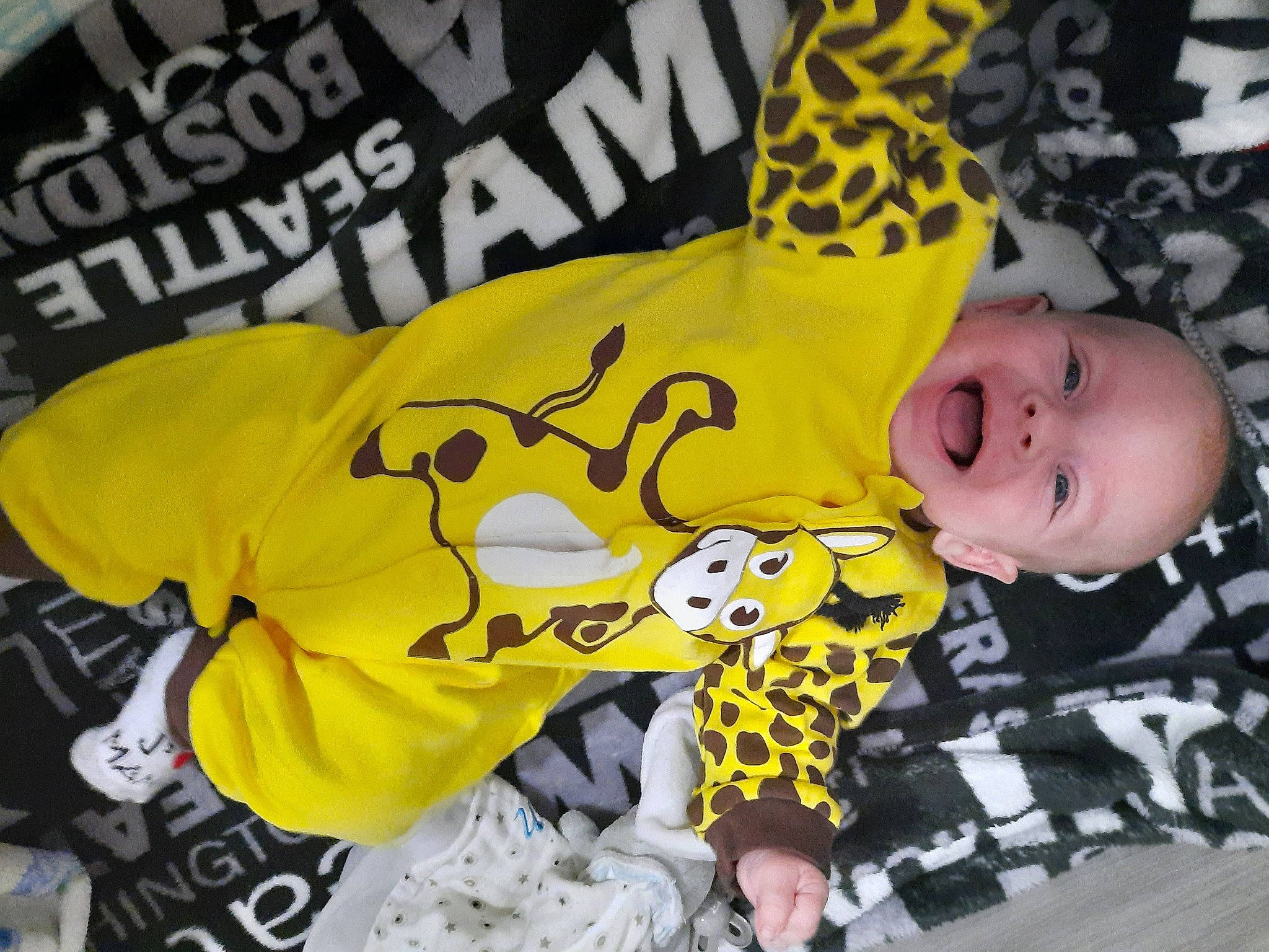 Zoran participe au concours pour gagner de l'argent avec cette photo : baby, baby_toddler_clothing, flooring, font, fun, happy, linens, logo, pattern, person, photo_caption, room, sleeve, smile, sportswear, t_shirt, textile, toddler, top, yellow