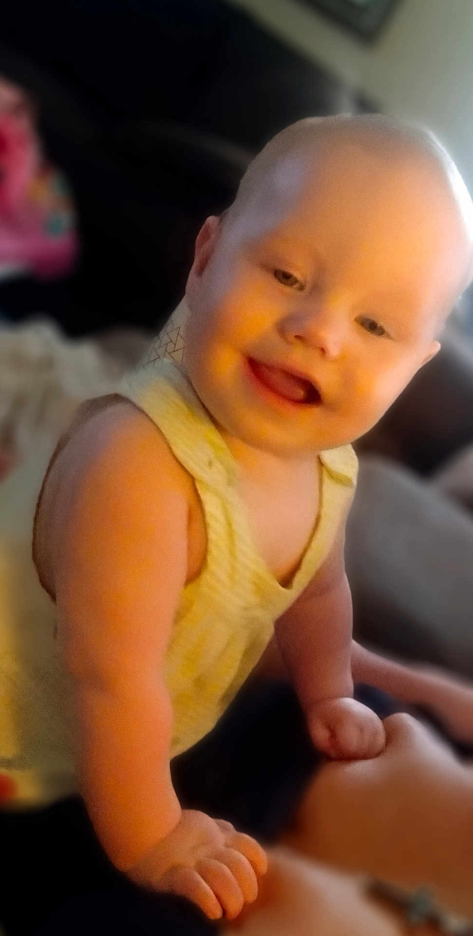 Evelyn is registered to the contest to win money with this photo: baby, smiling, happy, child, infant, face, skin, arm, hand, yellow_clothing, indoors, blurred_background, cute, portrait, young_child, person, sleeveless, light, expression, playful