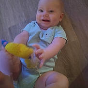 Evelyn is registered to the contest to win money with this photo: baby, child, smiling, onesie, toy, hand, floor, wooden_floor, happy, infant, cute, playful, person, skin, fingers, legs, casual_clothing, indoor, closeup, joy