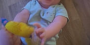 Evelyn is registered to the contest to win money with this photo: baby, casual_clothing, child, closeup, cute, fingers, floor, hand, happy, indoor, infant, joy, legs, onesie, person, playful, skin, smiling, toy, wooden_floor