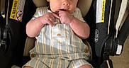 Waylon is registered to the contest to win money with this photo: baby, infant, car_seat, overalls, footwear, sandals, warning_label, child, cute, indoors, seat, person, sitting, looking, hands, fingers, clothing, head_support, safety, floor