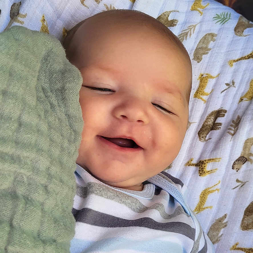 Noah is registered to the contest to win money with this photo: baby, bed, blanket, clothing, crib, cushion, face, furniture, happy, hat, head, homedecor, laughing, newborn, person, photography, portrait, quilt, smile, t_shirt