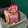 baby, stroller, infant, smiling, happy, hat, clothing, bottle, baby_lotion, toy, indoor, person, child, face, sitting, accessory, pink, gray, yellow, cute