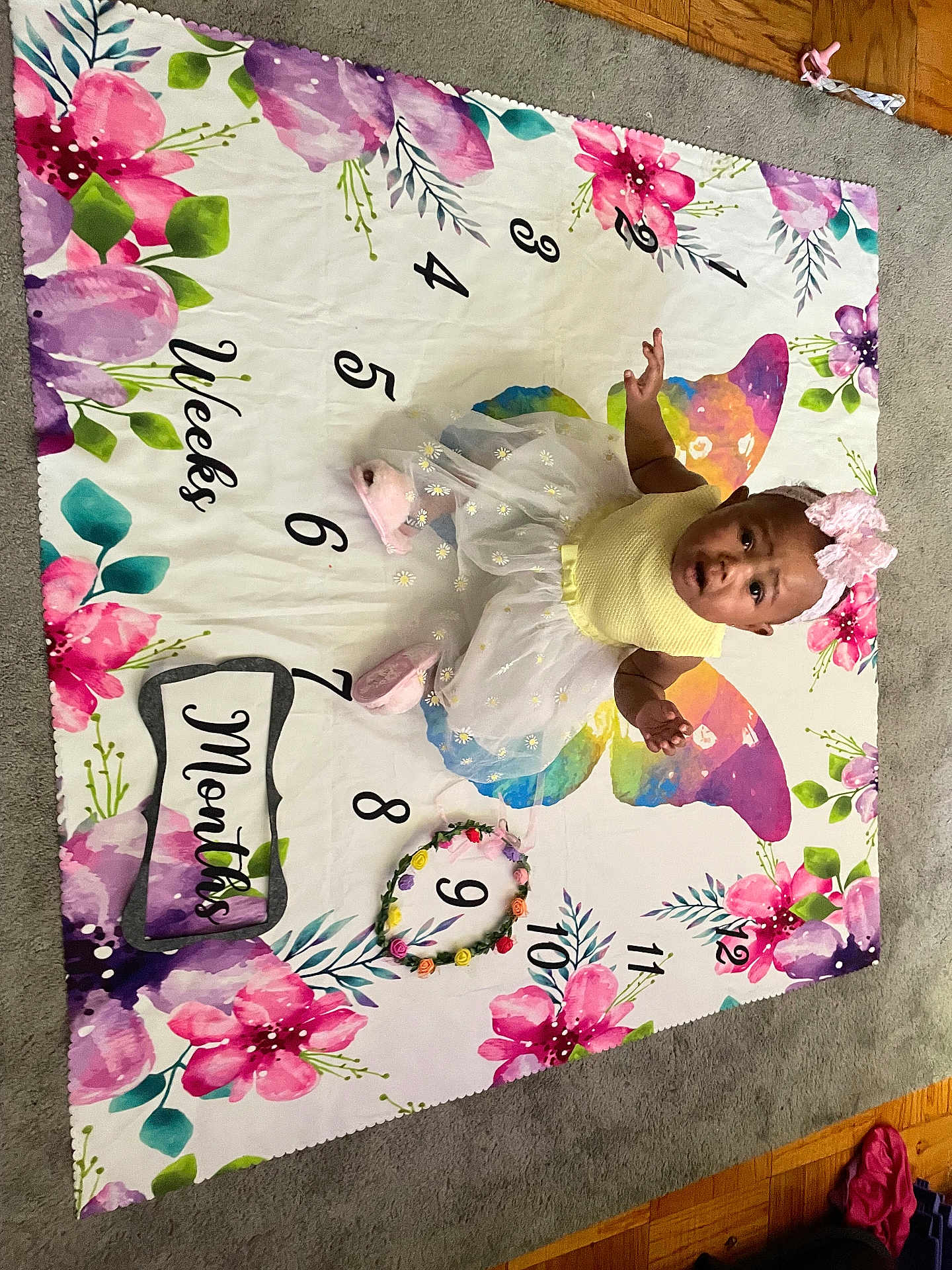 Jyleenia joined the competition — help win amazing prizes! baby, child, infant, milestone_blanket, flower_crown, pink_bow, yellow_top, white_tutu, pink_booties, sitting, carpet, wooden_floor, floral_pattern, colorful, milestone, months, weeks, portrait, indoor, cute