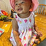 baby, child, pink_hat, strawberry_dress, smile, table, wooden_table, fruit_basket, envelope, chair, indoor, happy, cute, person, toddler, clothing, hat, face, skin, hand