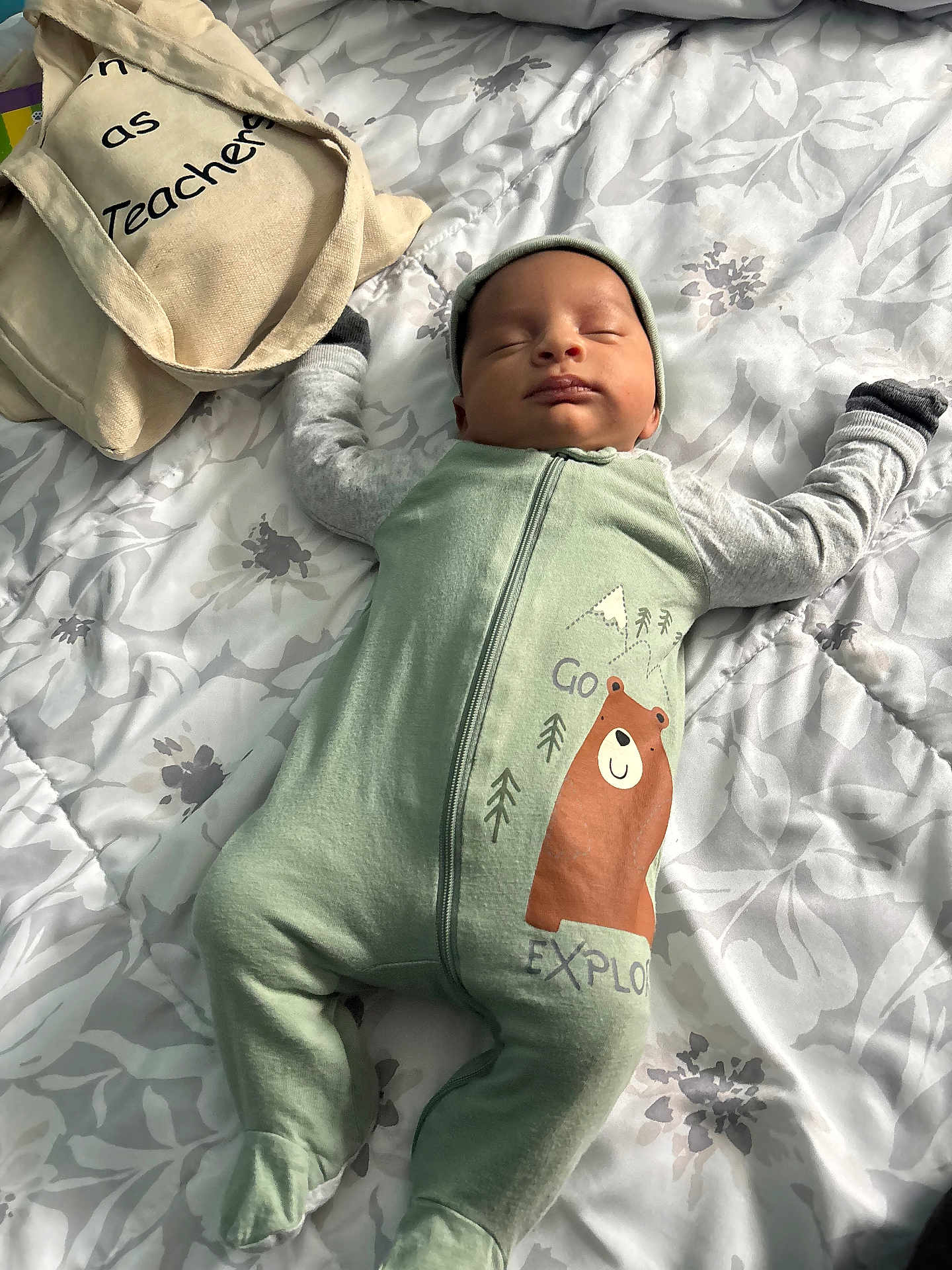 Idan is registered to the contest to win money with this photo: baby, infant, sleeping_baby, onesie, bear_graphic, hat, mittens, tote_bag, bed, blanket, floral_bedspread, zipper, peaceful, nap, indoors, soft_light, cute, newborn, fabric, patterned_bedding