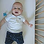 baby, crib, smiling, polo_shirt, shorts, pacifier, infant, happy, child, lying_down, wooden_bars, white_bed_sheet, blue, patterned_clothing, indoor, cute, young_child, person, baby_boy, nursery
