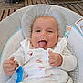baby, infant, tongue_out, white_clothing, baby_seat, pacifier, wooden_floor, smiling, cute, indoors, cozy, child, playful, comfort, seat, hands, head, face, patterned_clothing, relaxing