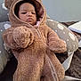 baby, child, teddy_bear_onesie, hooded_clothing, pillow, cloud_pattern, indoor, soft_texture, infant, face, cute, warm_clothing, seated, young_child, cozy, fabric, zipper, person, portrait, relaxed