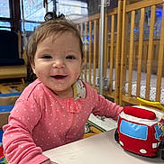 Allyana is registered to the contest to win money with this photo: baby, child, crib, daycare, drool, face, fire_truck, furniture, hand, happy, indoor, person, pink_clothing, play, plush_toy, polka_dot, smiling, table, toy, young_child