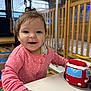 baby, child, crib, daycare, drool, face, fire_truck, furniture, hand, happy, indoor, person, pink_clothing, play, plush_toy, polka_dot, smiling, table, toy, young_child