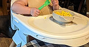 Jaxon is registered to the contest to win money with this photo: baby, bowl, elderly, facial_expression, feeding, food, glasses, happy, high_chair, ice_cube_tray, indoor, kitchen, messy, person, smile, spoon, table, tablecloth, whisk, wooden_floor